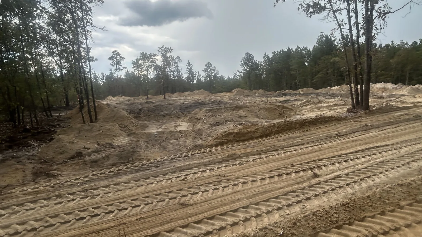 Cleared lot with sand piles and track marks under a cloudy sky, septic system installation