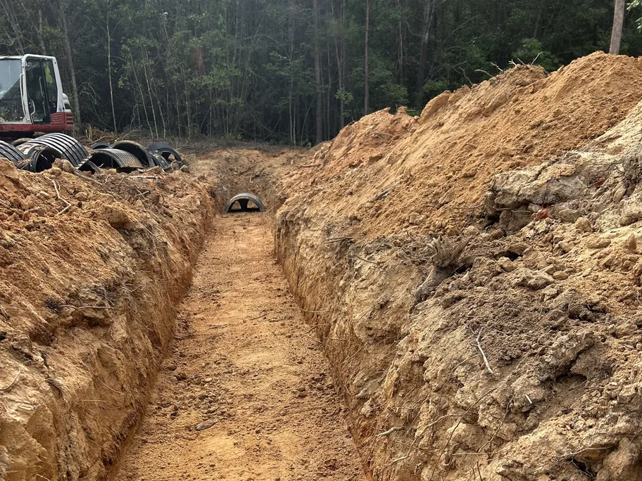 Dug trench with a chamber at the far end and an excavator by the woods, commercial septic systems
