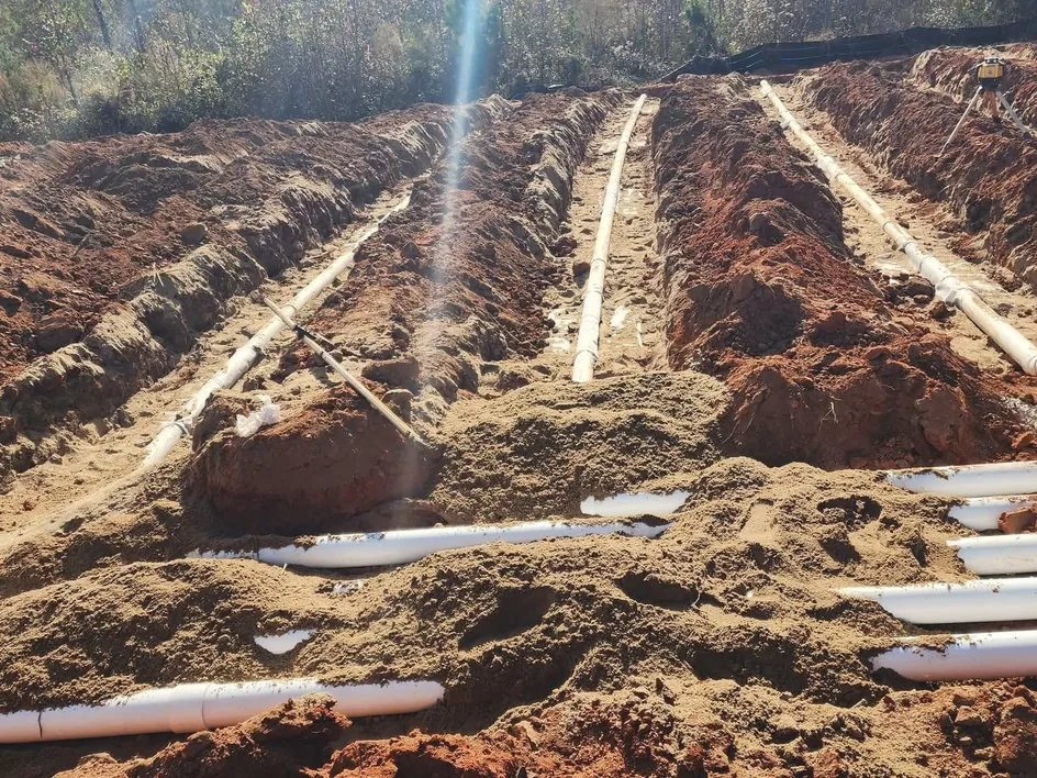 Parallel drain field trenches with white pipe laid in red clay and a laser level, commercial septic systems