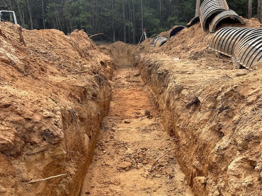 Drain field trench with chambers stacked on the bank and a laser level beyond, commercial septic systems