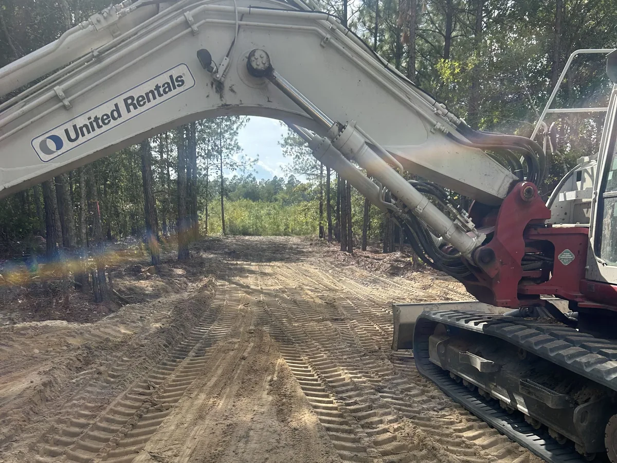 Excavator boom and tracks on a cleared dirt track in the pines, demolition