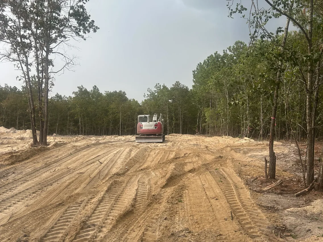 Excavator parked on freshly graded ground by the woods, demolition