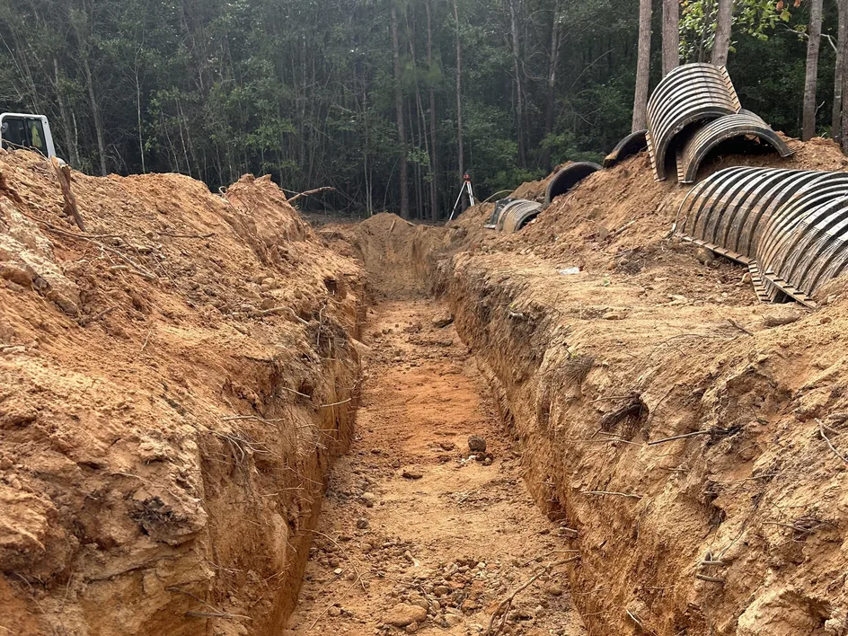 Freshly dug drain field trench with chambers stacked on the bank and a laser level beyond, drain field repair