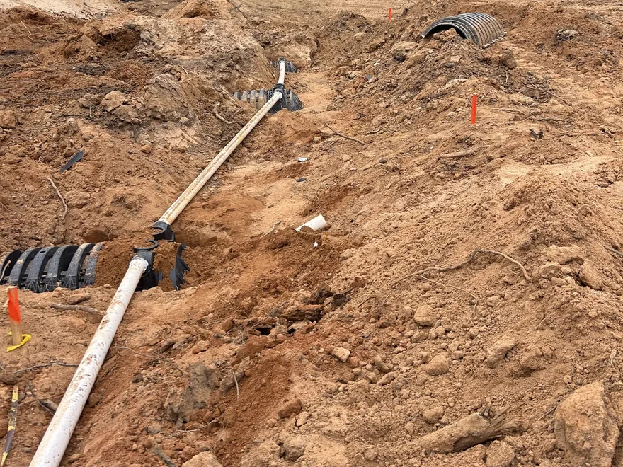 PVC line feeding the drain field chamber rows with marker flags in the dug soil, drain field repair