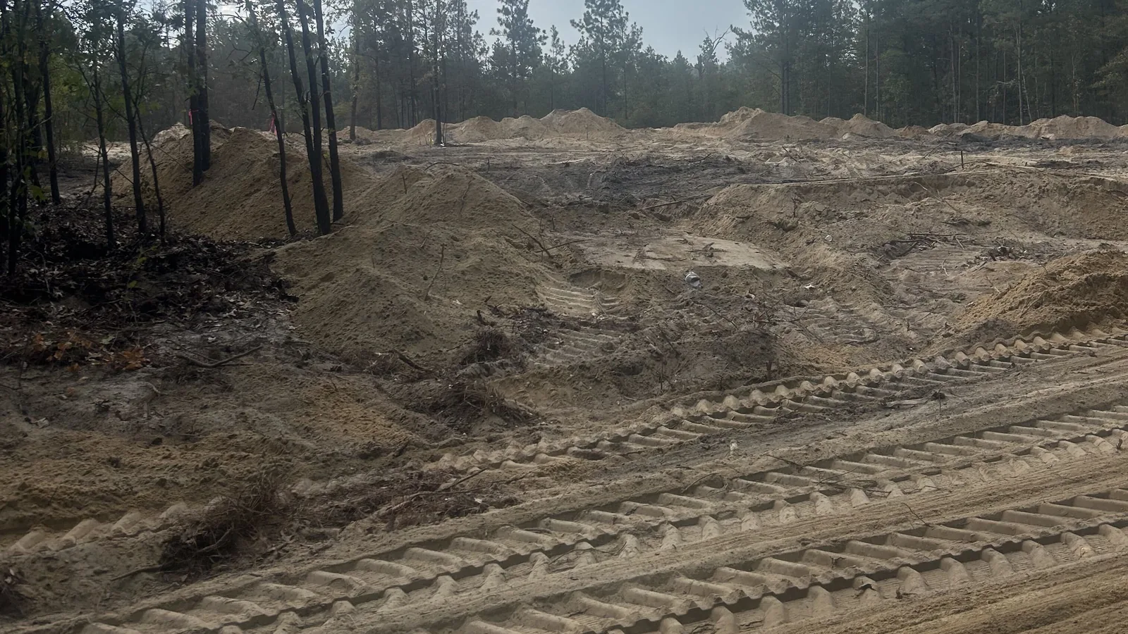 Freshly cleared ground with sand piles and track marks, septic system installation