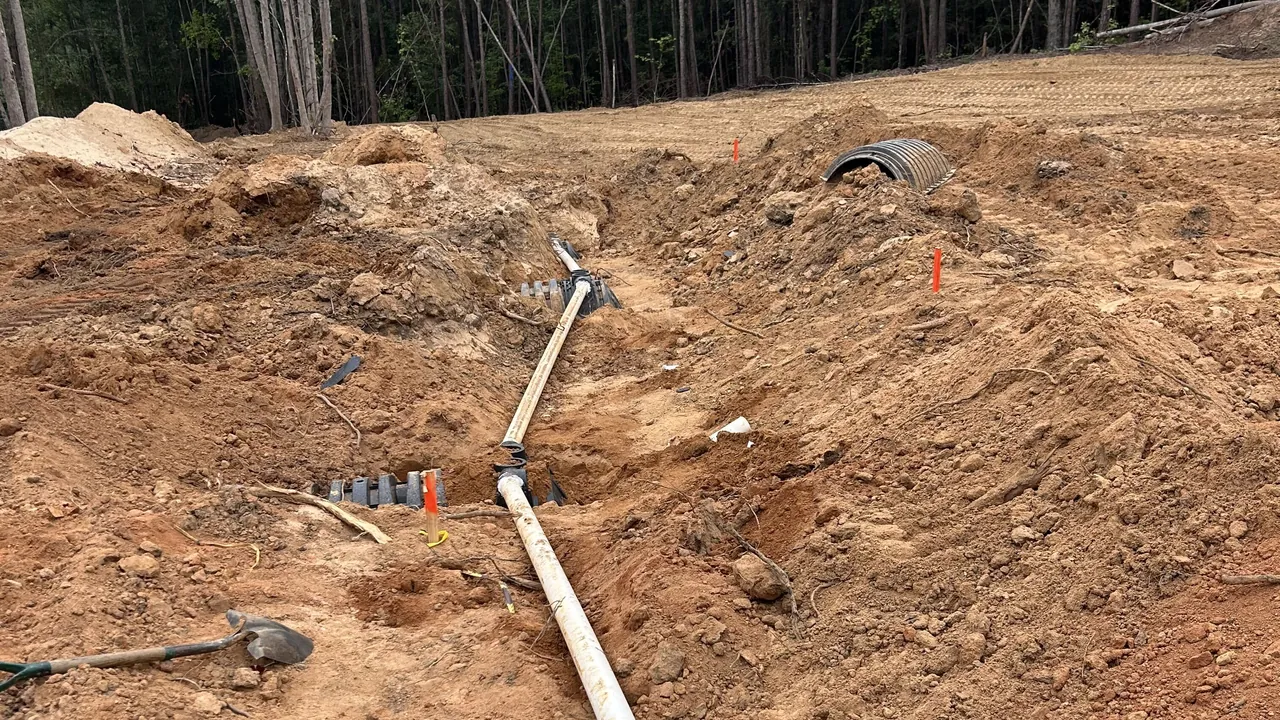 PVC septic line laid through a dug trench to the drain field chambers on a cleared lot, septic system installation