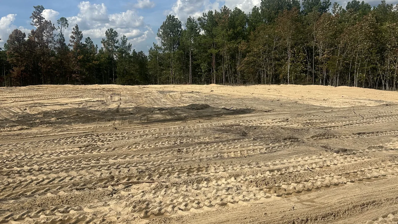 Cleared sandy lot below the pine tree line, septic system installation