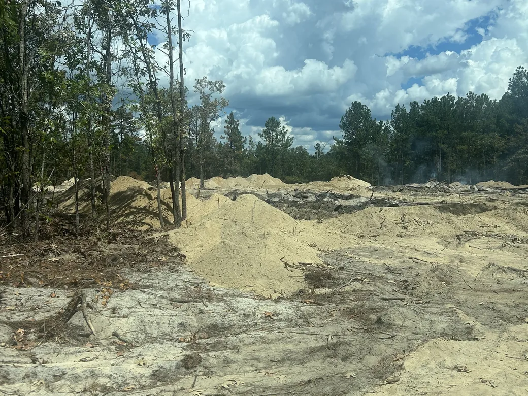 Sand piles and smoldering debris on a lot being cleared, lot clearing