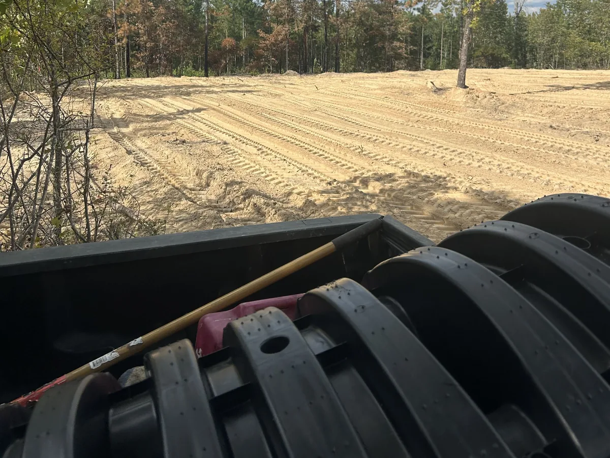 Stacked drain field chambers and tools on a truck facing a cleared lot, septic system repair