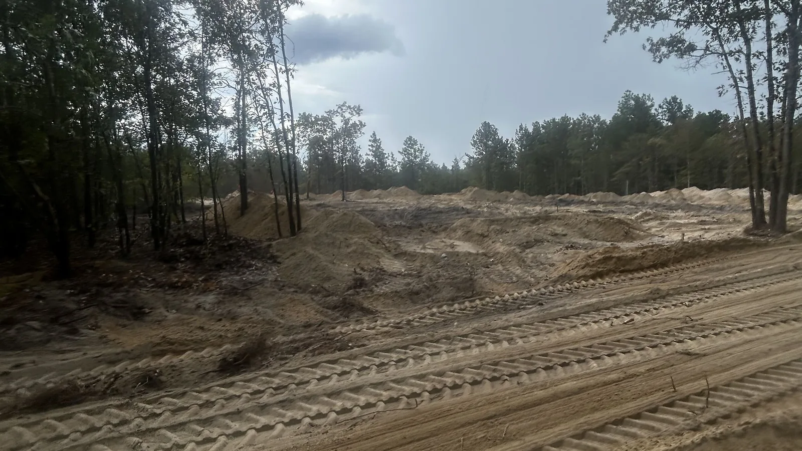 Cleared lot with sand piles and track marks along the tree line, septic system installation